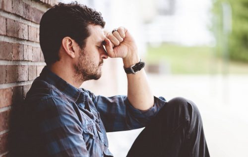 A depressed guy sitting by the wall with hand on head